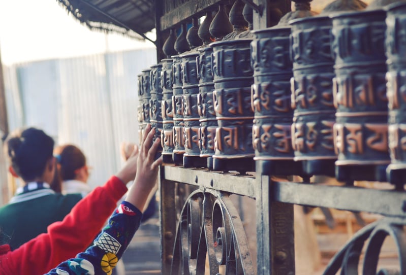 Unrecognizable pilgrims touching Prayer wheels in ancient temple in Nepal